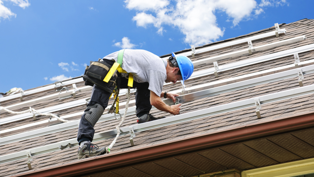 A worker installing custom flexible solar panel mounts on a sloped roof for an energy-efficient setup.